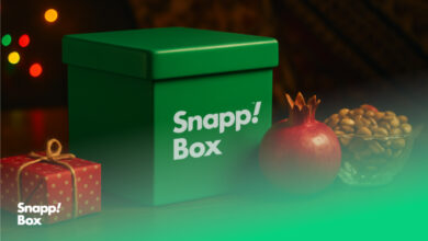 باکس سبز اسنپ‌باکس در کنار سفره‌ی یلدا شامل آجیل، انار و یک کادوی قرمز